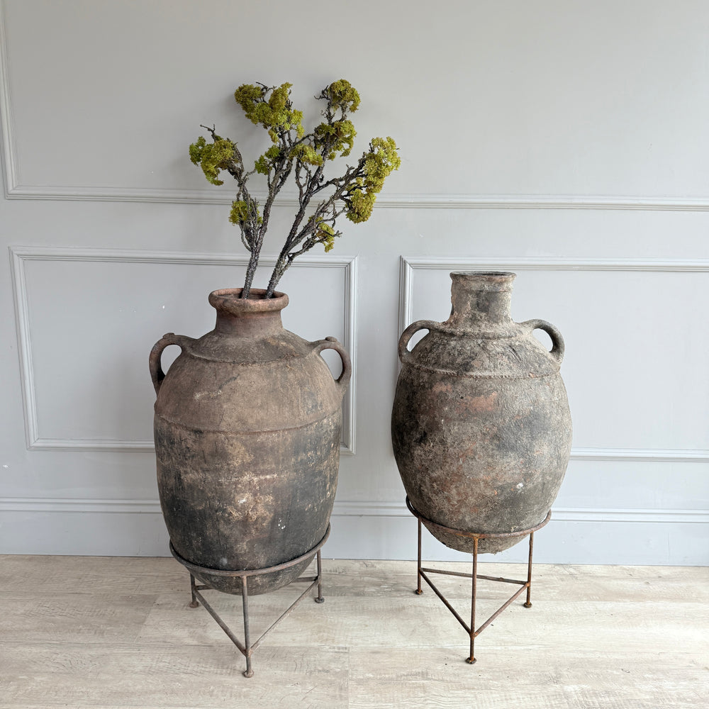 Two large rustic vases with a plant against a light gray wall.