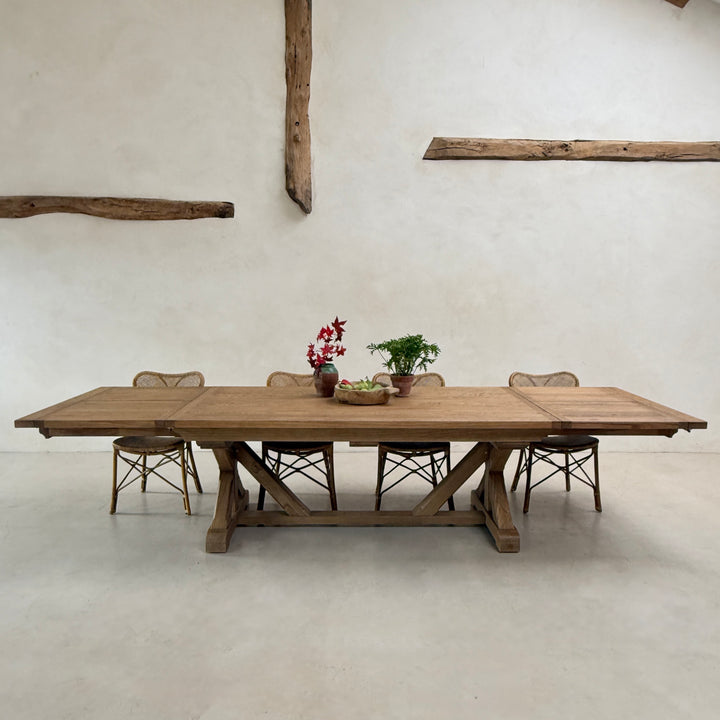 Front view of the substantial reclaimed oak extending dining table showing its architectural cross-frame base and natural timber finish.