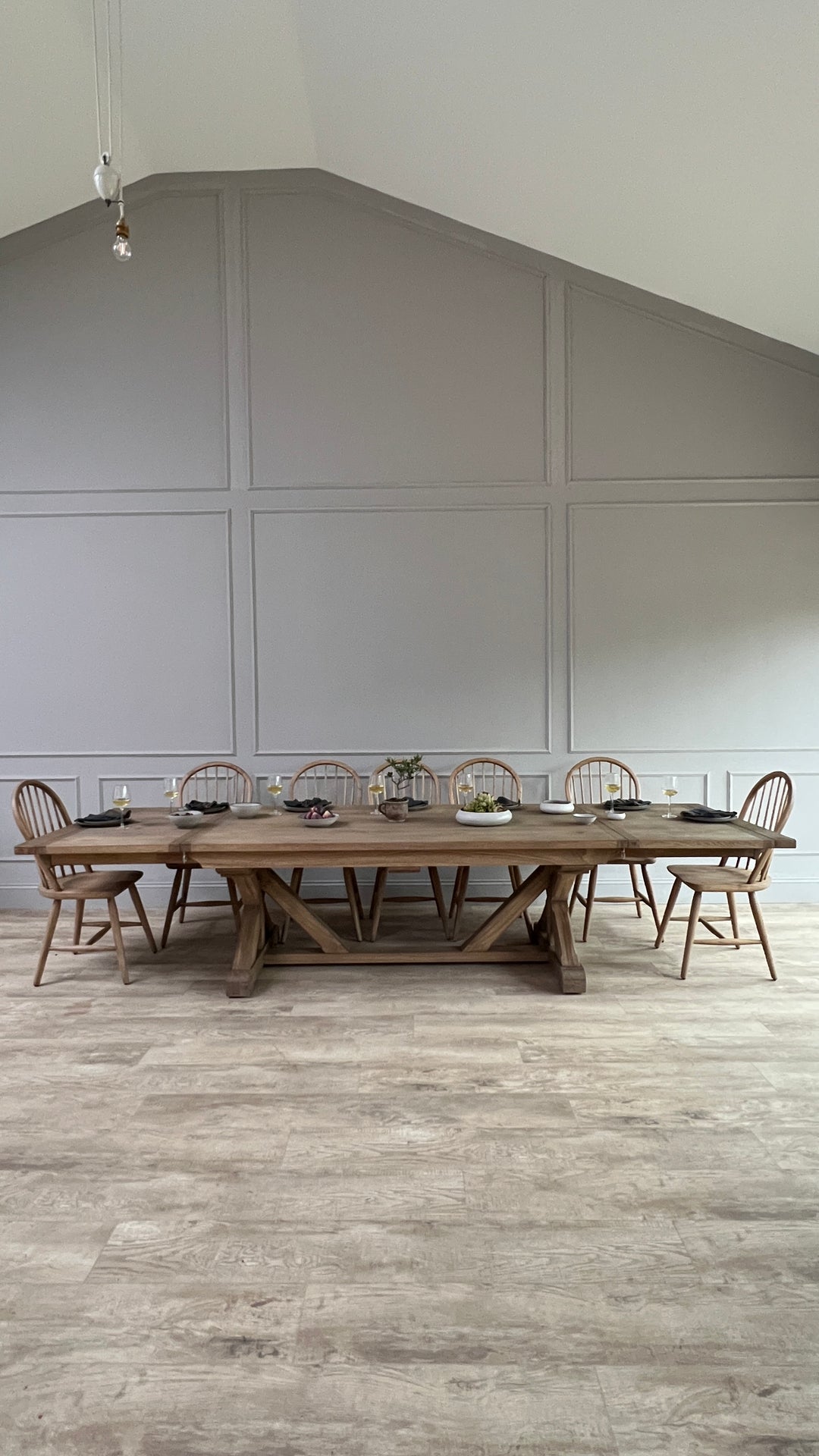 Full-length view of a large reclaimed oak extending dining table styled with Windsor chairs in a pared-back contemporary interior. The generous scale, handcrafted trestle base and characterful reclaimed timber highlight the table&