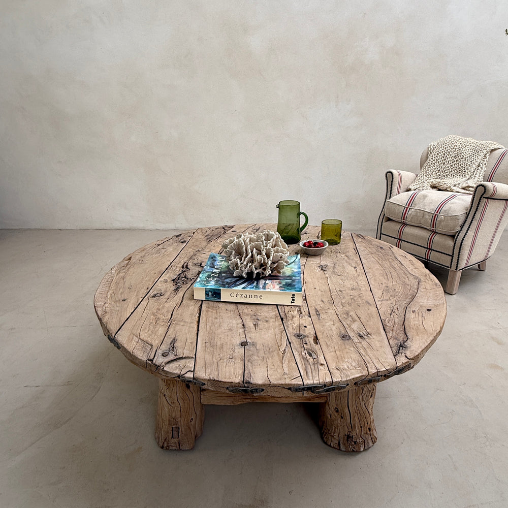 Round wooden table with decorative items in a room with a chair and light-colored floor.