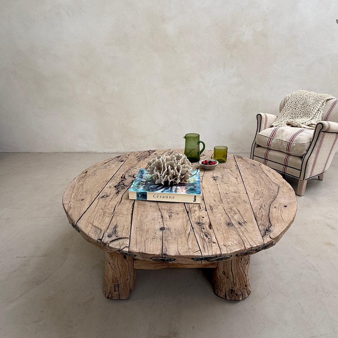 Round wooden table with decorative items in a room with a chair and light-colored floor.