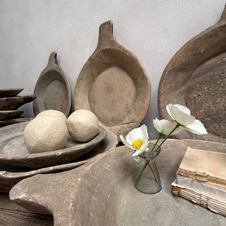 Collection of rustic stone bowls and a vase with flowers on a gray surface.
