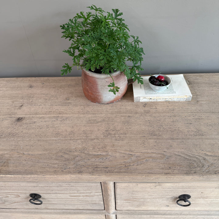 Wooden dresser with a potted plant and small bowl on top against a gray wall.