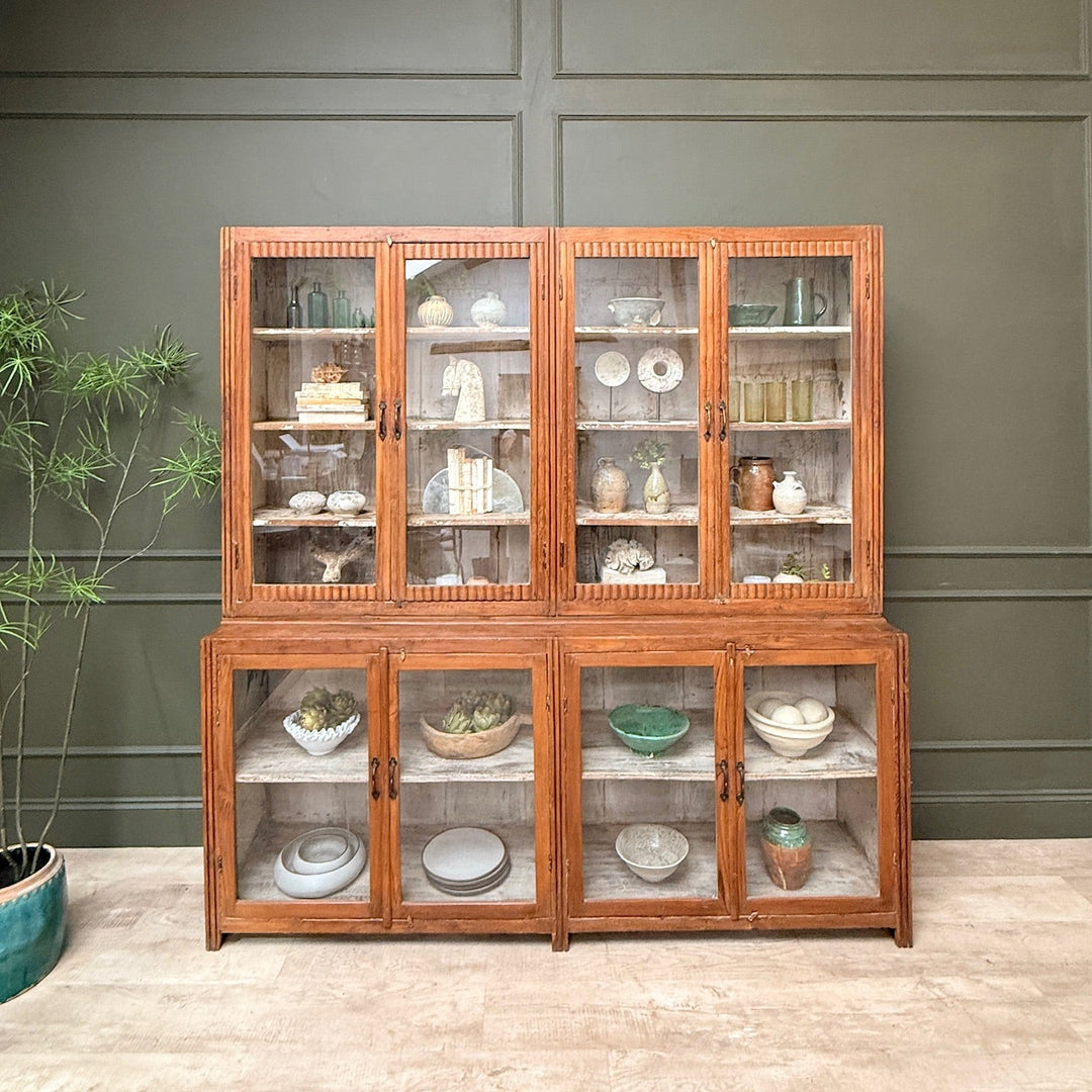 Wooden display cabinet with glass doors against a green wall