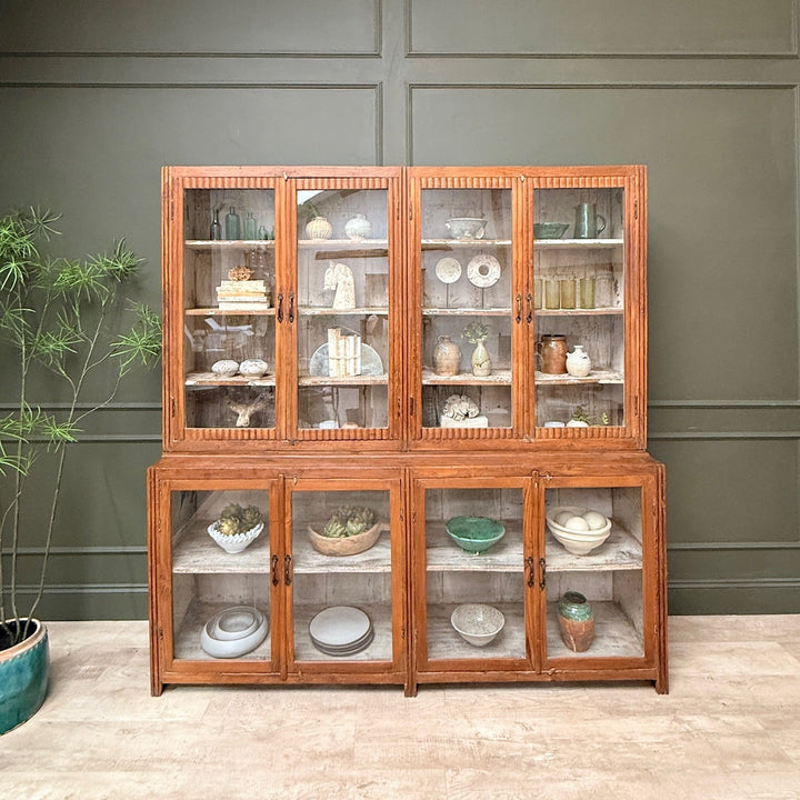 Wooden display cabinet with glass doors against a green wall