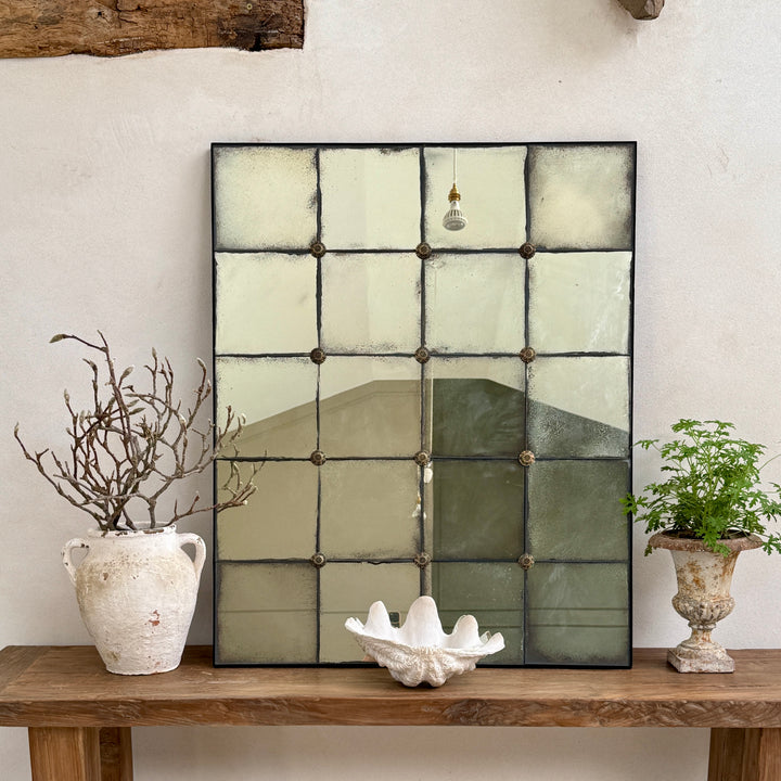 Leonora large foxed antiqued window mirror with hand-distressed Verre Églomisé glass and decorative brass rosettes, styled on a reclaimed teak console table in a contemporary country home.