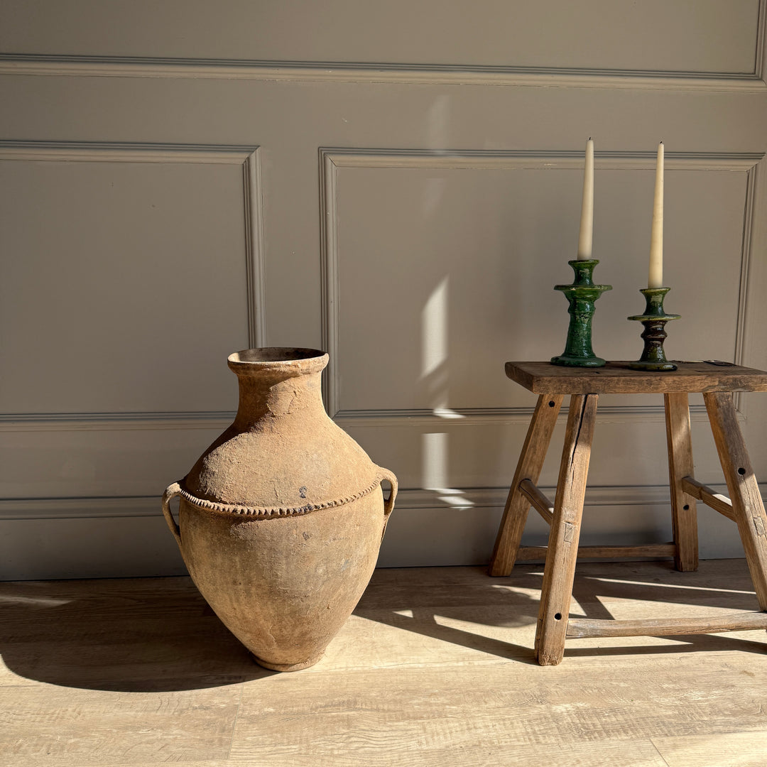 Large terracotta pot on a wooden floor with a small wooden table and candlesticks in the background.