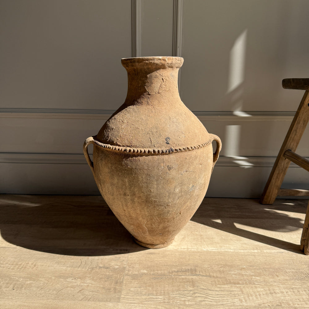 Large brown ceramic vase on a wooden floor with a neutral wall background