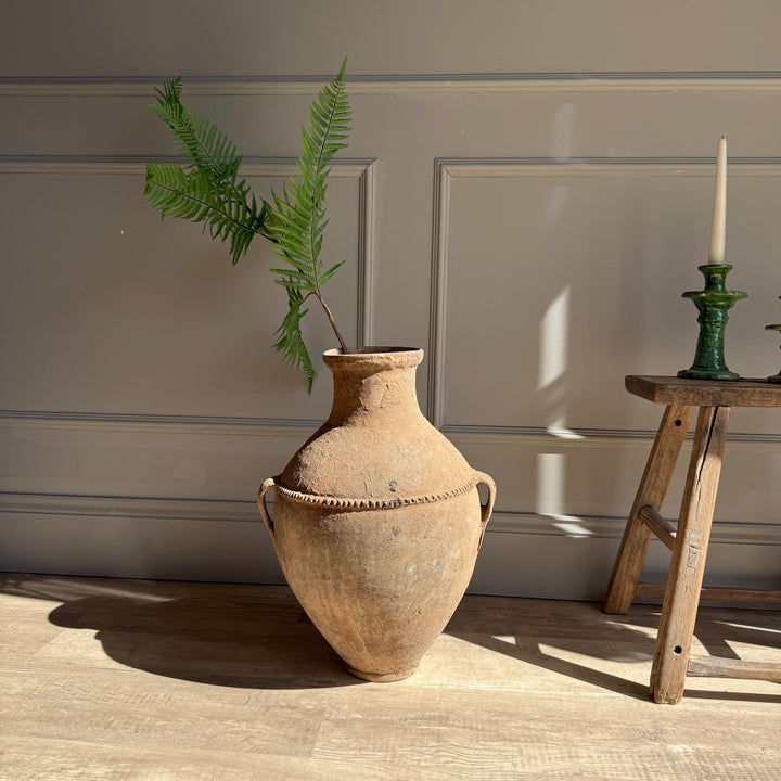 Vintage-style vase with a plant against a neutral wall