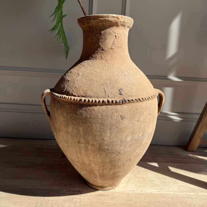 Vintage terracotta pot with rope handles on a wooden surface