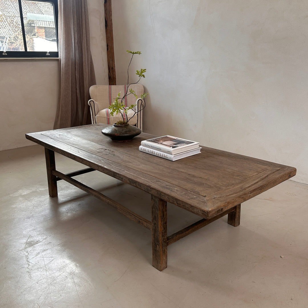 styled view of the Reclaimed Elm Coffee Table with a ceramic vase and books, highlighting the generous tabletop and understated craftsmanship. The reclaimed elm grain and softly weathered finish bring warmth and texture to contemporary and rustic interiors.