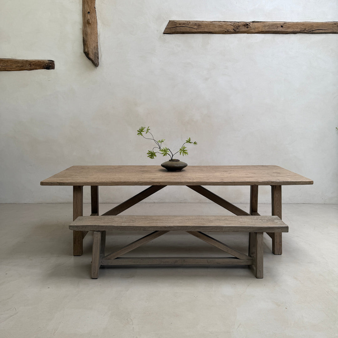The Reclaimed Elm Farmhouse Dining Table Cambridge with matching bench, photographed in a pared-back farmhouse interior. Crafted from salvaged elm timber with distinctive grain, natural variation and timeless proportions, this handcrafted dining table brings understated elegance to contemporary country and modern rustic homes.