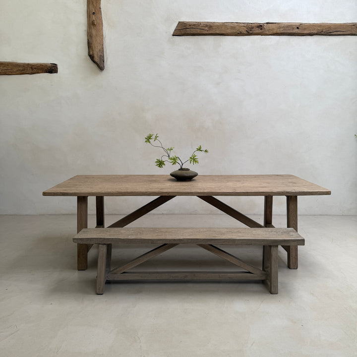 The Reclaimed Elm Farmhouse Dining Table Cambridge with matching bench, photographed in a pared-back farmhouse interior. Crafted from salvaged elm timber with distinctive grain, natural variation and timeless proportions, this handcrafted dining table brings understated elegance to contemporary country and modern rustic homes.