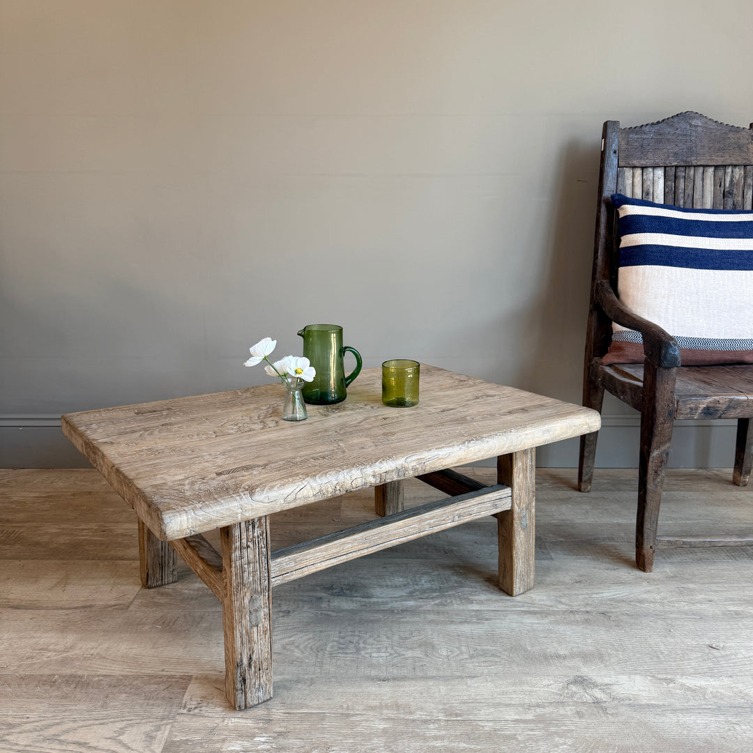 Wooden table with decorative items in a room with a chair and striped cushion.