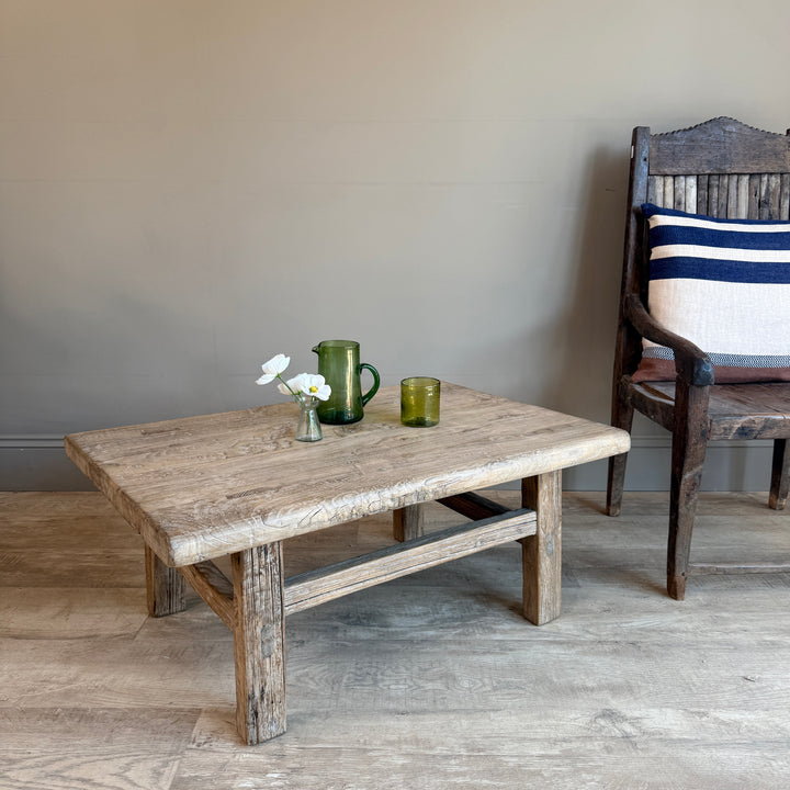 Wooden table with decorative items in a room with a chair and striped cushion.