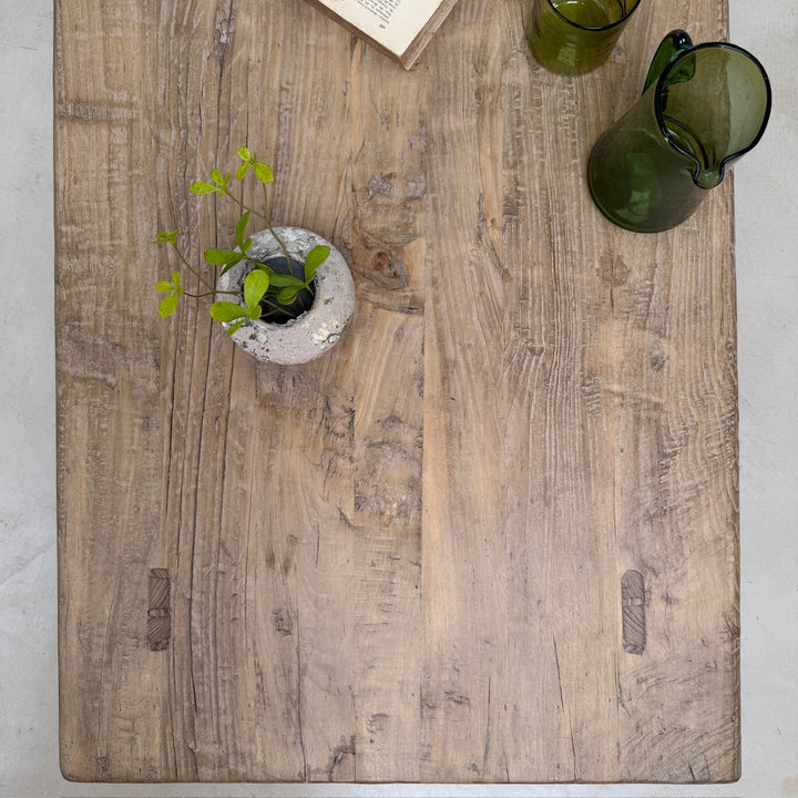 Wooden cutting board with a plant and green glass on a light gray surface