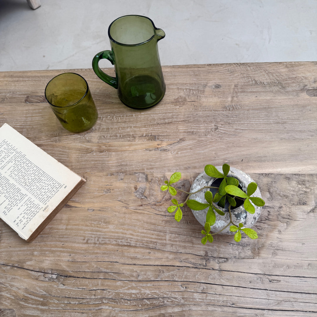 Green glass pitcher and cup on a wooden surface with a small plant and open book.
