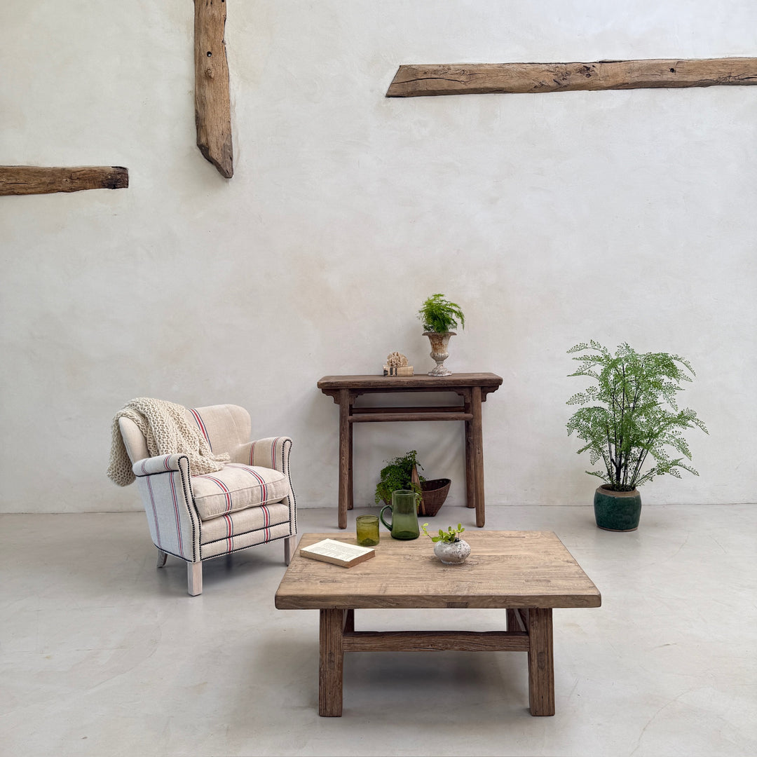 Cozy living room with wooden furniture, armchair, and plants against a white wall.