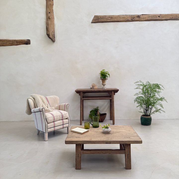 Cozy living room with wooden furniture, armchair, and plants against a white wall.