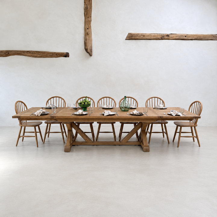 Large solid reclaimed American oak extending dining table styled with wooden spindle back chairs in a contemporary barn interior.