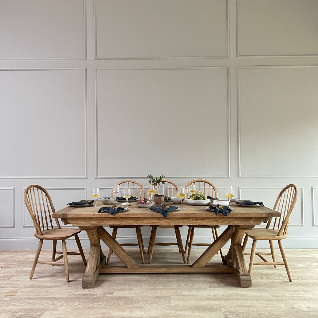 The Reclaimed Oak Extending Dining Table styled for relaxed entertaining with Windsor dining chairs, artisan tableware and seasonal serving dishes. Crafted from characterful reclaimed oak, the substantial trestle base and generous proportions highlight the natural beauty of salvaged timber, creating a timeless dining space suited to contemporary country interiors and modern family living.