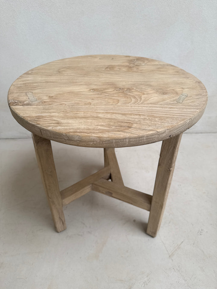 Wooden stool with round seat and four legs on a light gray floor.
