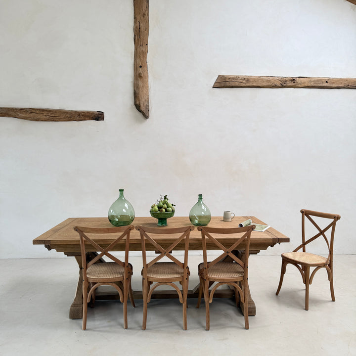 Characterful reclaimed wood dining table surrounded by cross-back dining chairs and styled with green glass vessels.