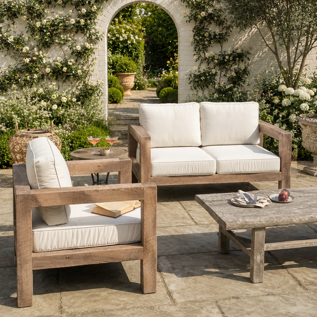 Outdoor patio furniture set with wooden frames and white cushions in a garden setting.
