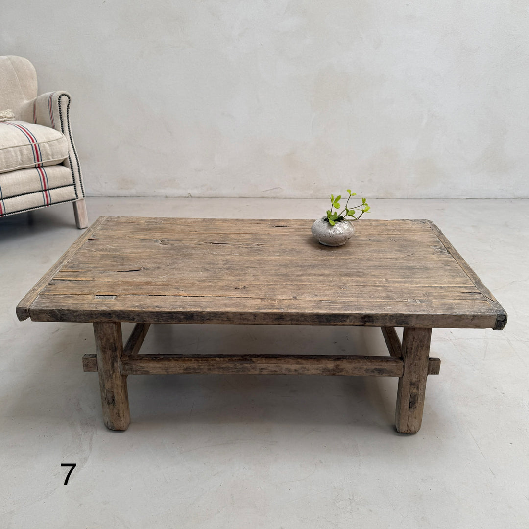Wooden coffee table with a vase on a gray floor and wall.
