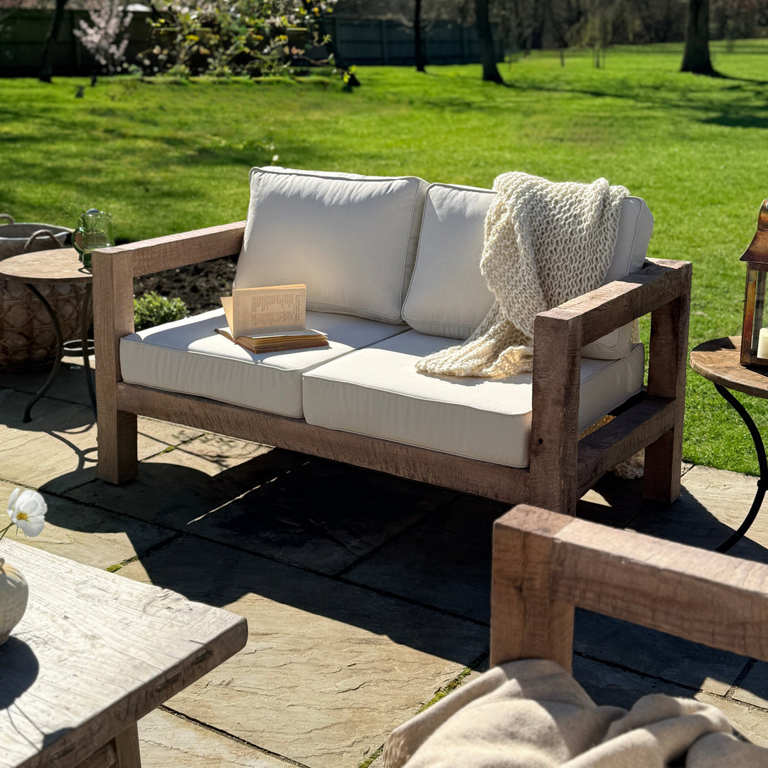 Outdoor patio with wooden sofa, cushions, and a blanket on a sunny day.