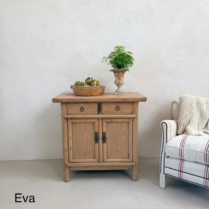 Wooden side table with decorative items next to a chair with a plaid cover on a plain background