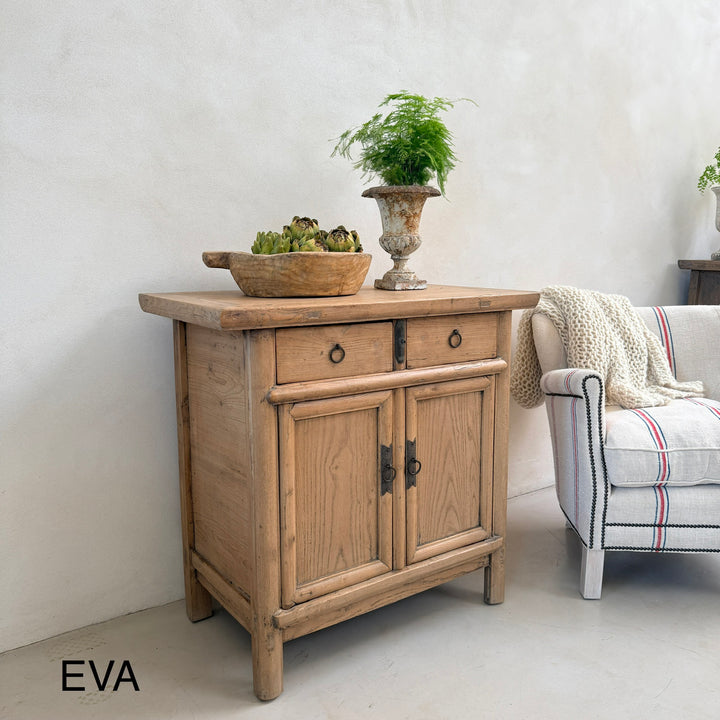 Wooden sideboard with decorative items in a room with a sofa and plants.