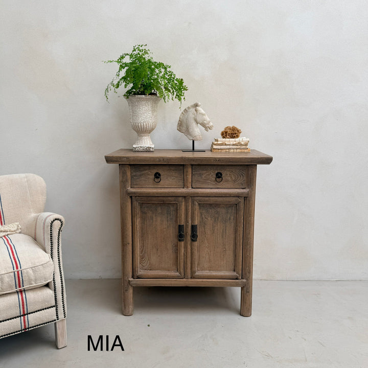Wooden side table with decorative items against a plain wall, next to a plaid armchair.