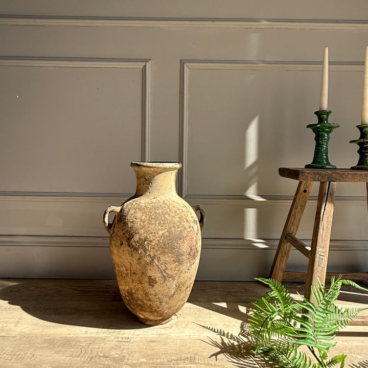 Vintage-style vase on a wooden floor with a neutral wall background