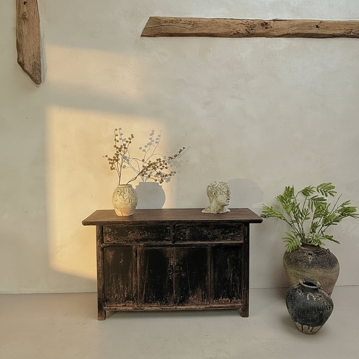 Vintage wooden cabinet with decorative items against a plain wall.