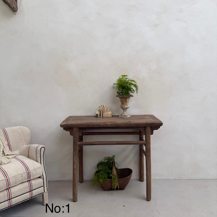 Wooden table with decorative items against a white wall, next to a plaid armchair.