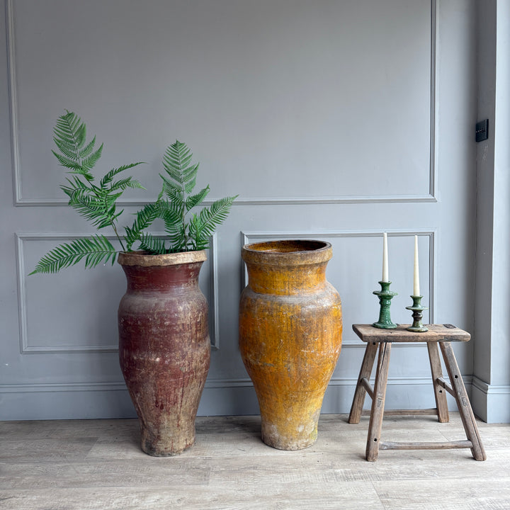 Two large ceramic vases with a plant and candles on a small wooden stool against a gray wall.