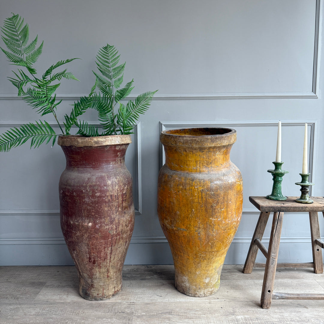 Two large rustic vases with a plant and candles on a wooden stool against a gray wall.