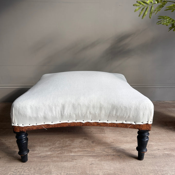 Antique French upholstered footstool with a softly padded cream seat, curved wooden frame and dark turned legs, matching deconstructed armchair Louise.