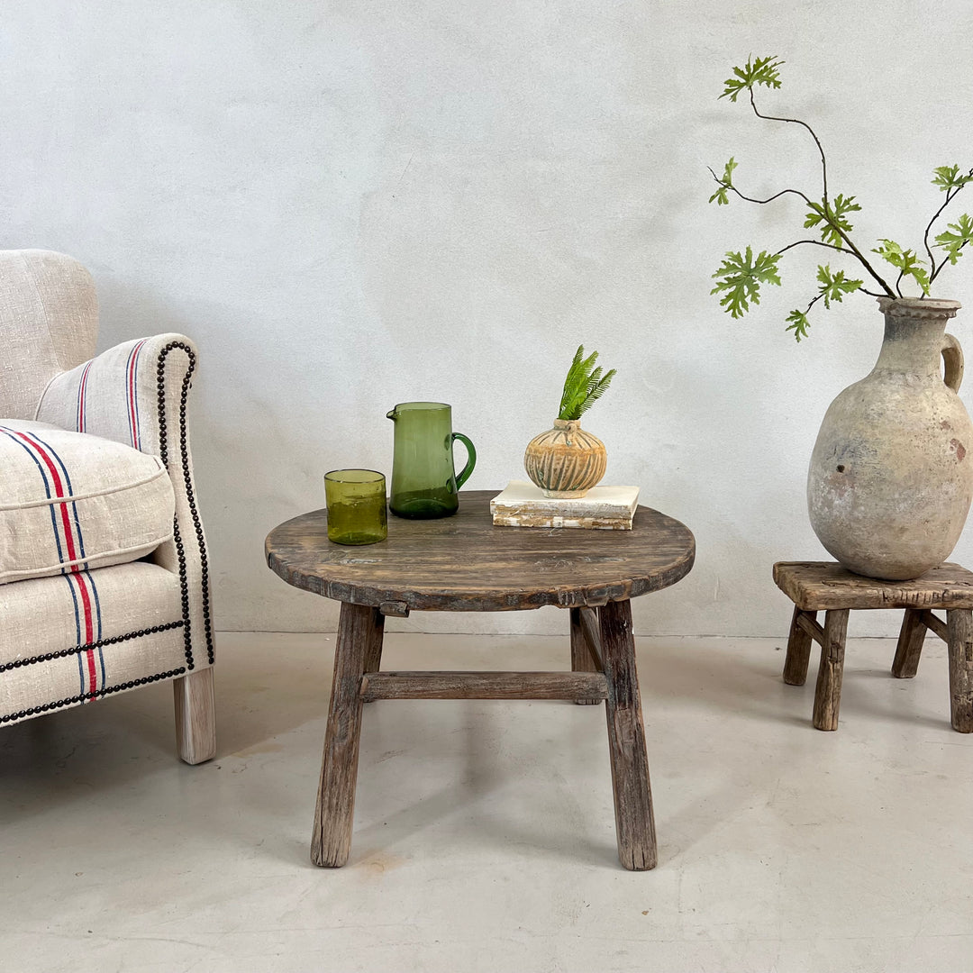 Antique Round Elm Side Table Morgana styled beside a linen armchair with decorative accessories in a modern rustic living room.

