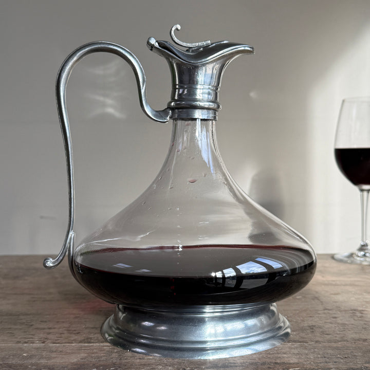 Side view of a French glass red wine decanter featuring a wide rounded body, pewter pedestal base and elegant curved pouring handle.