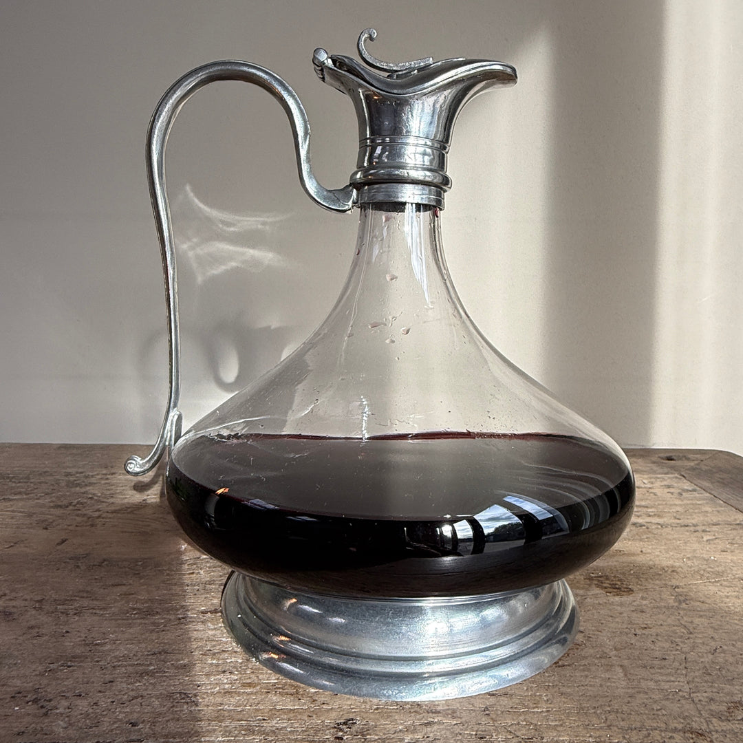 Full front view of a French pewter and glass wine decanter, showcasing its elegant silhouette, wide glass body, curved handle and decorative metal base.