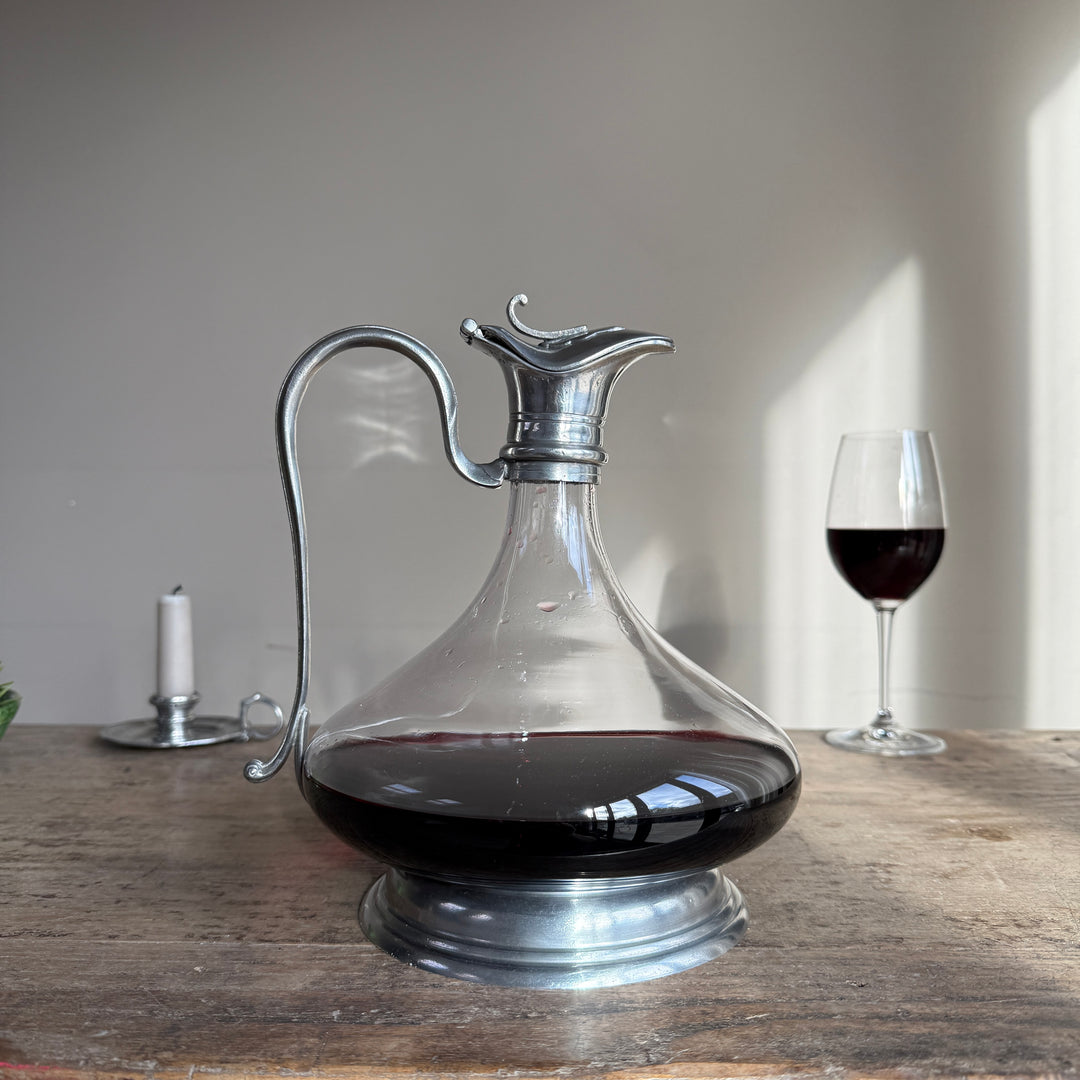 French pewter and glass wine decanter with an elegant curved metal handle, decorative pouring spout and pewter pedestal base, displayed with red wine.