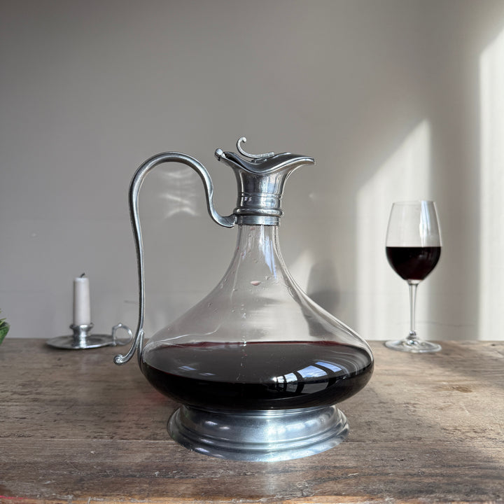 French pewter and glass wine decanter with an elegant curved metal handle, decorative pouring spout and pewter pedestal base, displayed with red wine.