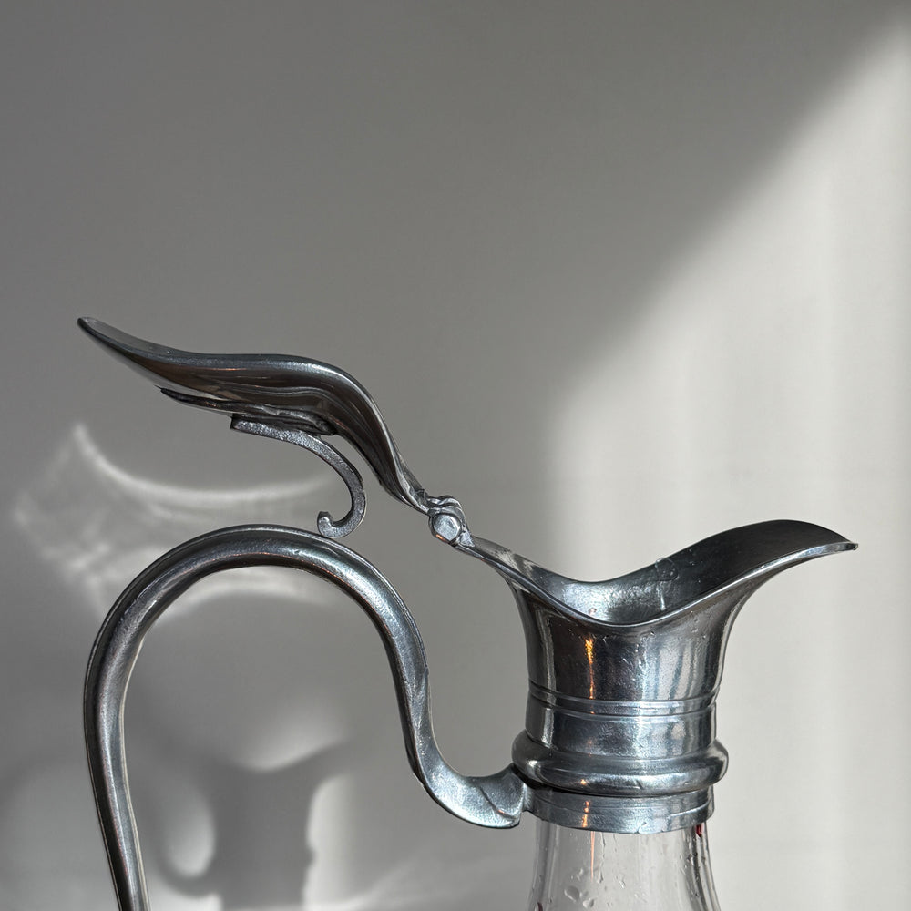Close-up of the sculptural pewter pouring spout and curved handle on a traditional French glass wine decanter.