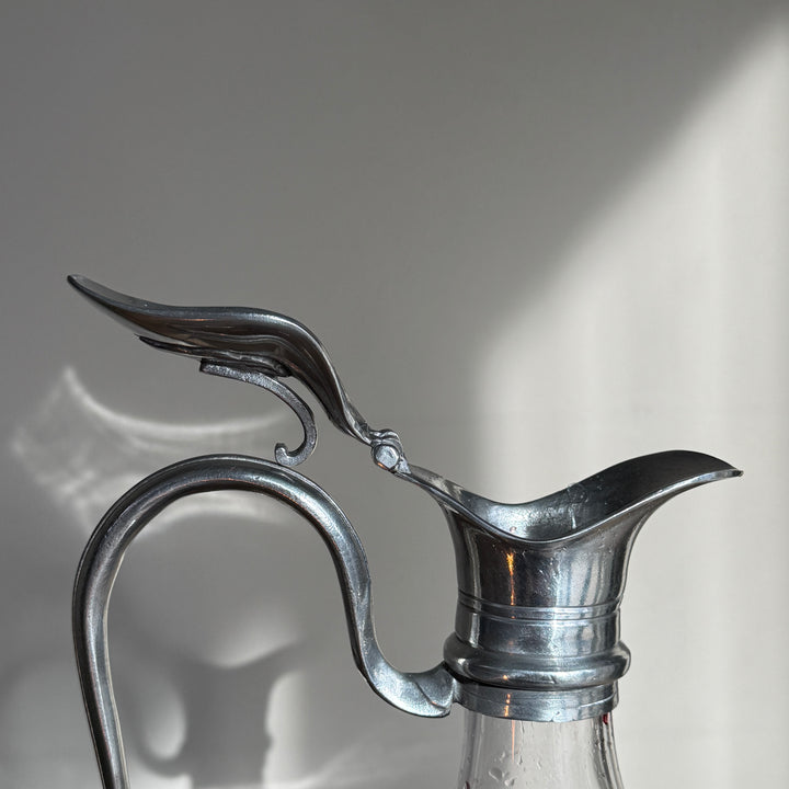 Close-up of the sculptural pewter pouring spout and curved handle on a traditional French glass wine decanter.