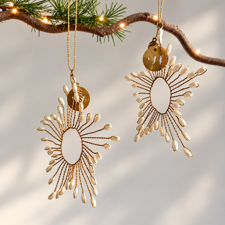 ornate gold-toned hanging ornaments with circular medallions and radiating pearl bead-like strands, suspended from a tree branch with warm string lights against a soft light gray background.  Home Barn Christmas decoration collection 