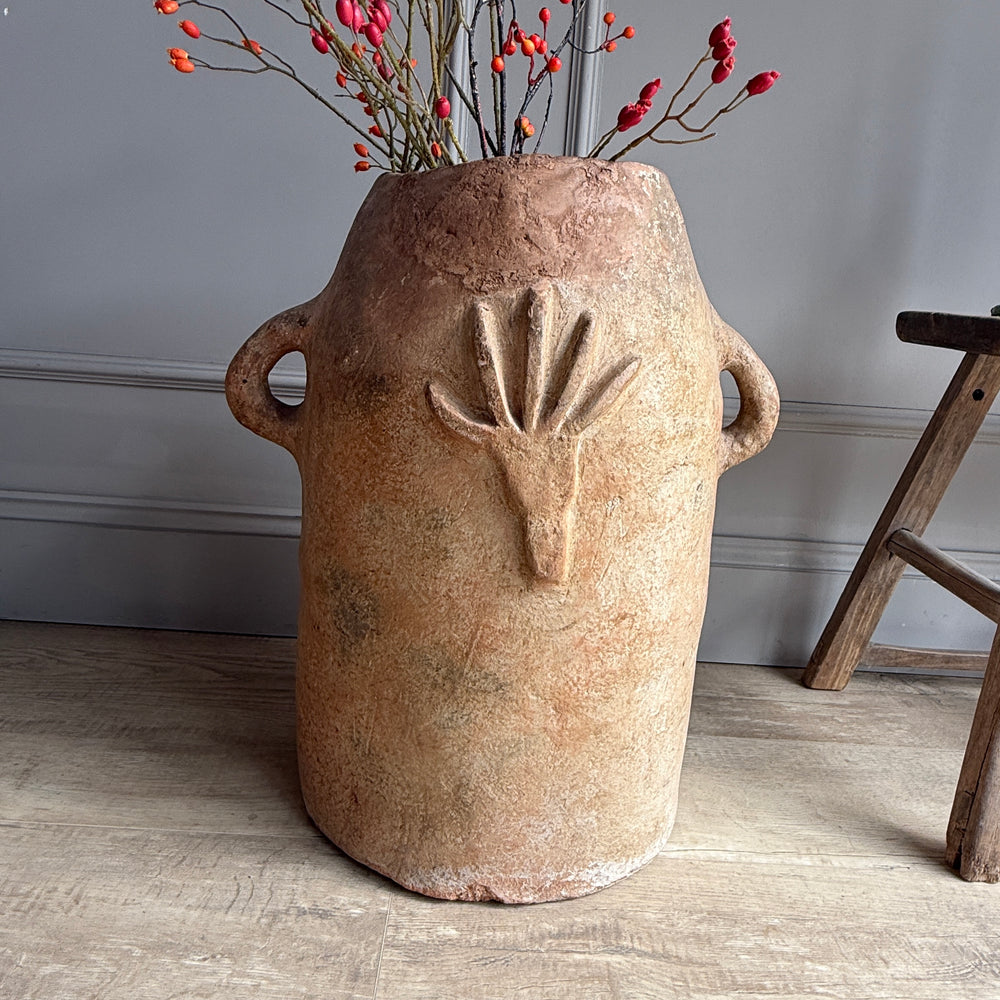 Ceramic vase with face design and dried flowers on a wooden floor