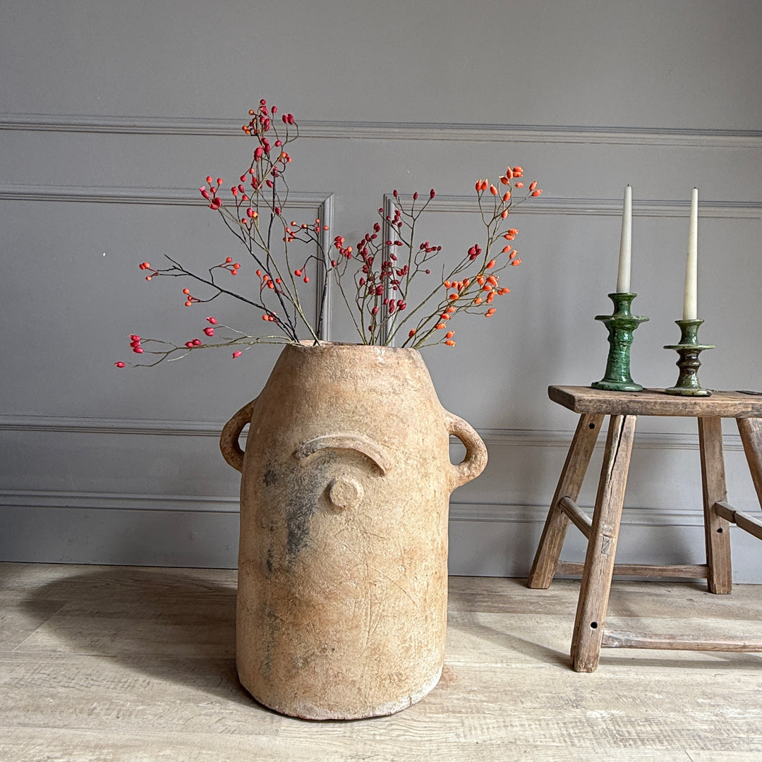 Decorative vase with branches and berries on a wooden floor against a gray wall.