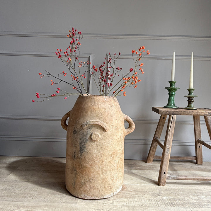 Decorative vase with branches and berries on a wooden floor against a gray wall.